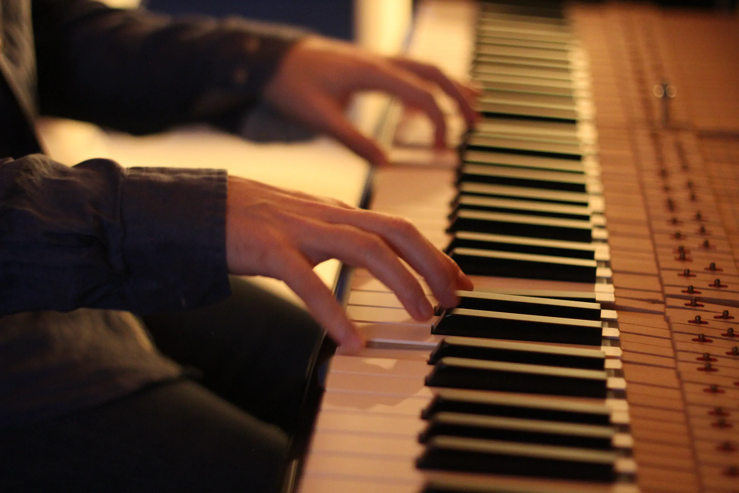 Dettaglio delle mani di Michele Bargigia sui tasti del pianoforte in luce calda.