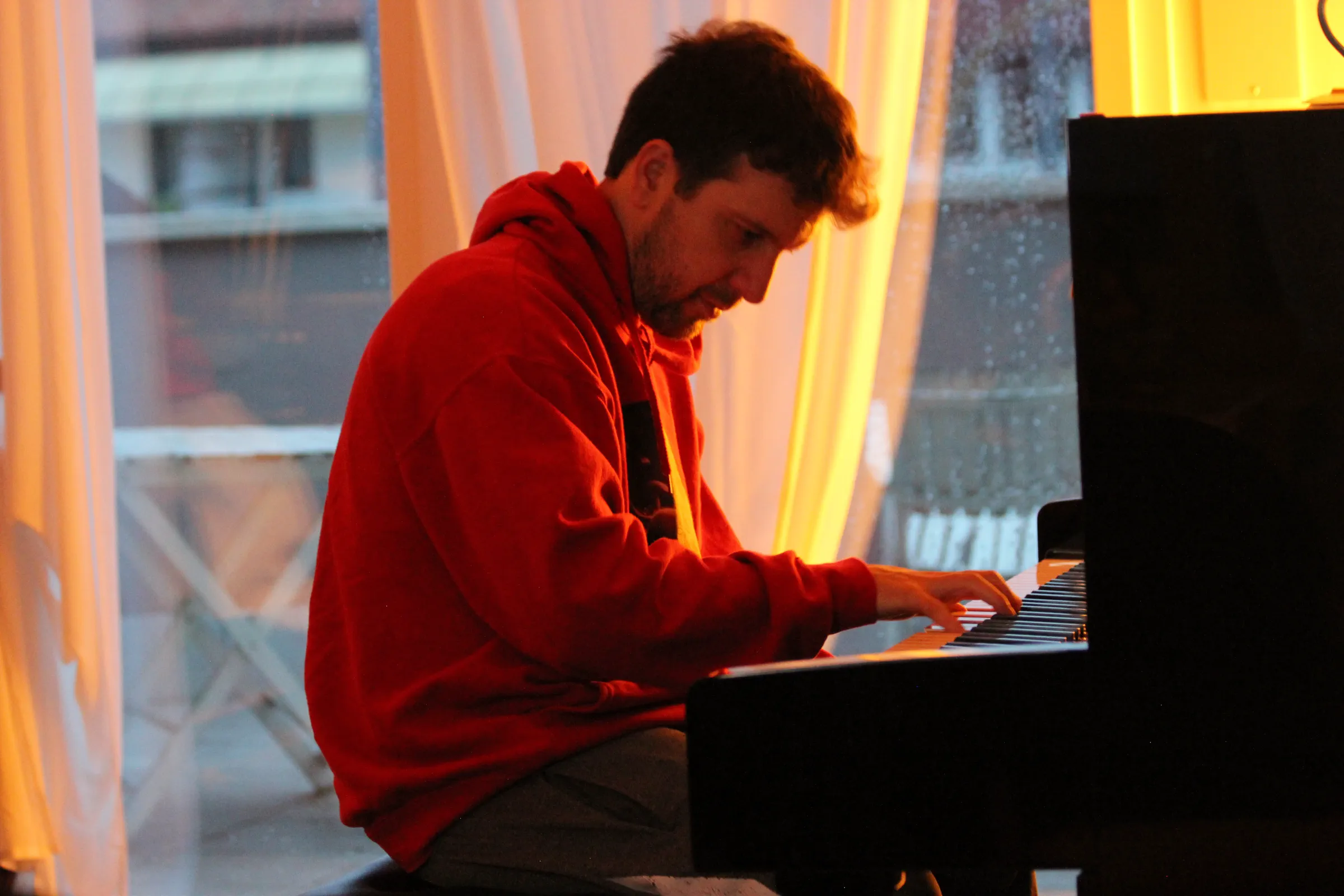 Michele Bargigia al pianoforte in studio con una felpa rossa.