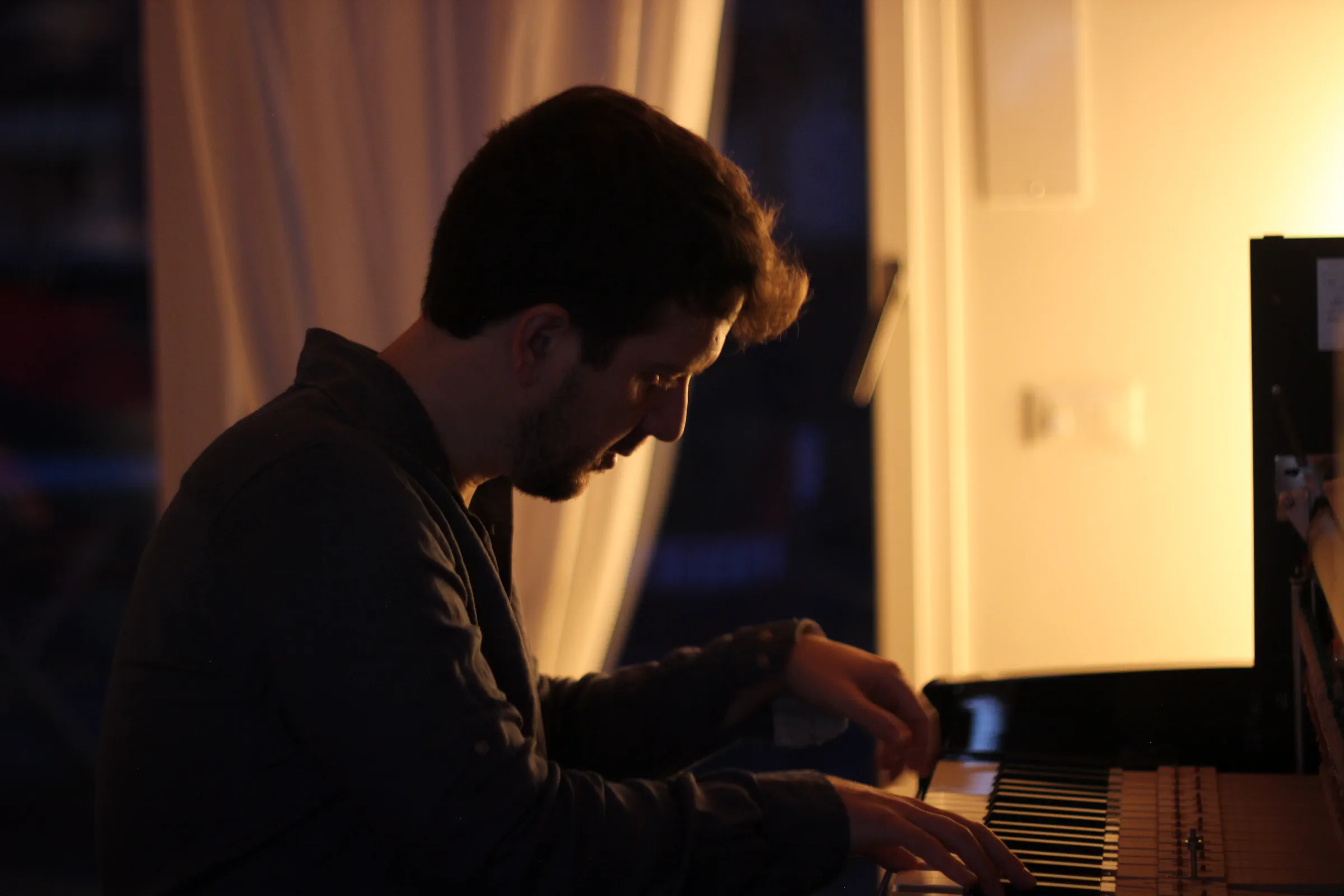 Silhouette di Michele Bargigia seduto al pianoforte davanti a una finestra.